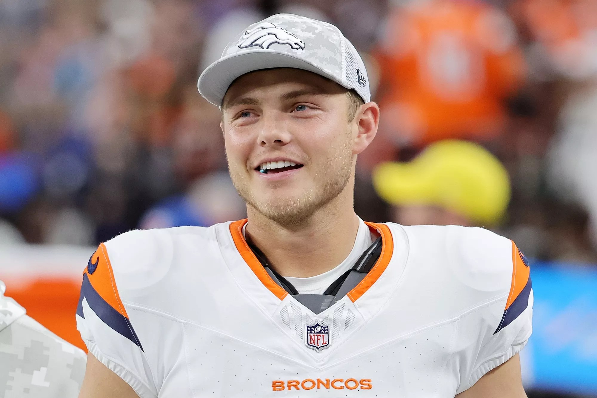 Candid photo of a smiling Zach Wilson #4 of the Denver Broncos in uniform but wearing a team ballcap and looking on during the third quarter of a game against the Las Vegas Raiders at Allegiant Stadium  in Las Vegas, Nevada, on November 24, 2024.
