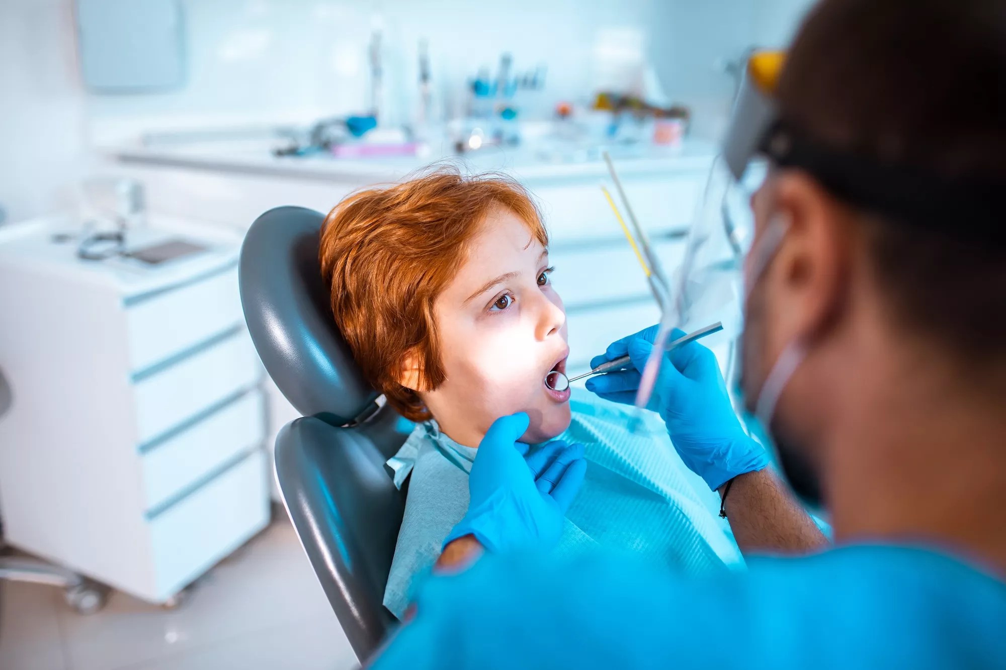 Young boy in a dentists office having work done on his teeth by a male dentist