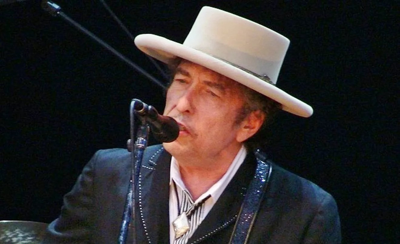 headshot of an older bob dylan performing, sporting a wide-brimmed hat